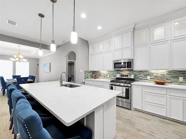 kitchen with sink, stainless steel appliances, a kitchen breakfast bar, a center island with sink, and decorative light fixtures