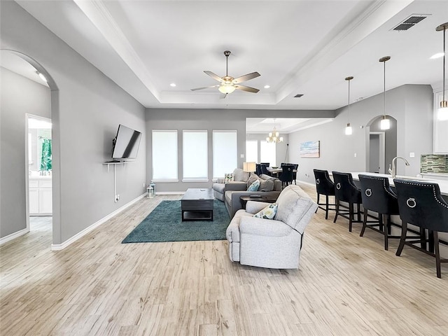 living room with a tray ceiling, ceiling fan with notable chandelier, and light wood-type flooring