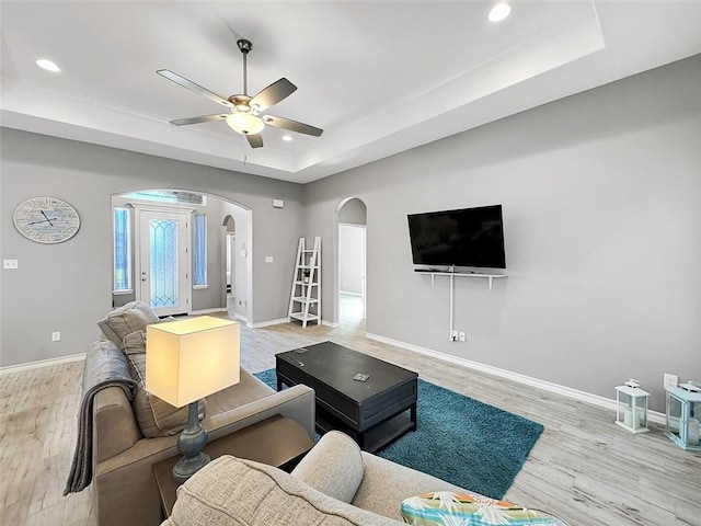 living room with a raised ceiling, ceiling fan, and light hardwood / wood-style flooring