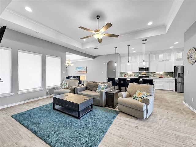 living room with ornamental molding, a tray ceiling, and ceiling fan with notable chandelier