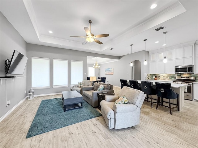 living room with a raised ceiling, ceiling fan with notable chandelier, and light hardwood / wood-style floors