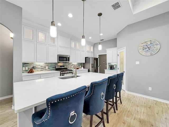 kitchen with hanging light fixtures, appliances with stainless steel finishes, sink, and a kitchen island with sink