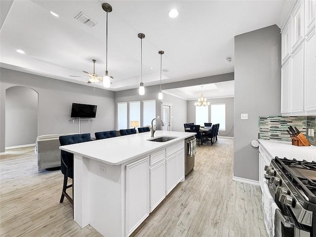 kitchen with appliances with stainless steel finishes, a breakfast bar, an island with sink, sink, and a tray ceiling