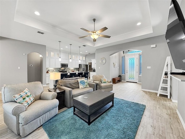 living room featuring ceiling fan, a raised ceiling, and light hardwood / wood-style flooring