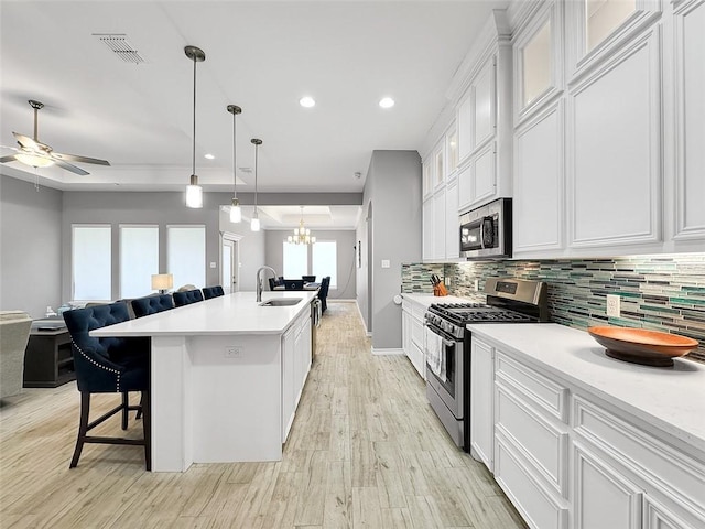 kitchen with a kitchen bar, sink, white cabinetry, appliances with stainless steel finishes, and an island with sink