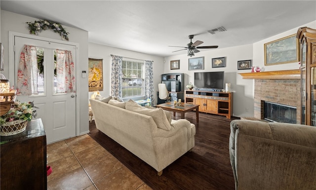 living room featuring a brick fireplace, dark tile patterned flooring, and ceiling fan