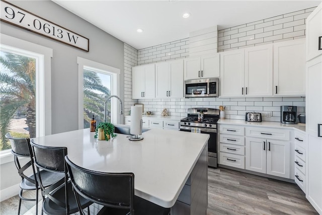 kitchen with white cabinets, backsplash, an island with sink, and stainless steel appliances