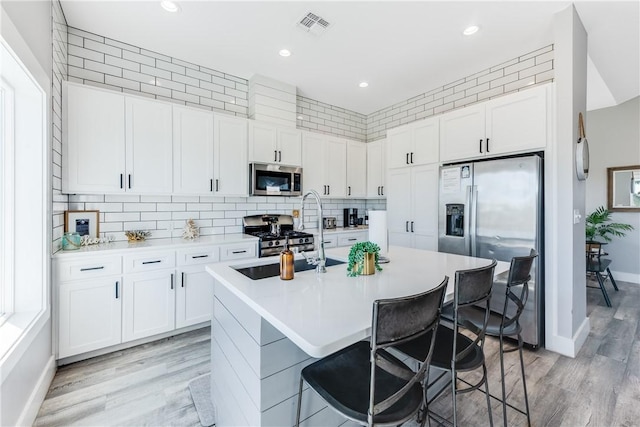 kitchen with white cabinets, a center island with sink, stainless steel appliances, and a breakfast bar area