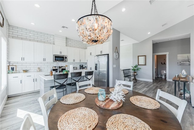 dining space featuring sink, light hardwood / wood-style flooring, lofted ceiling, and an inviting chandelier