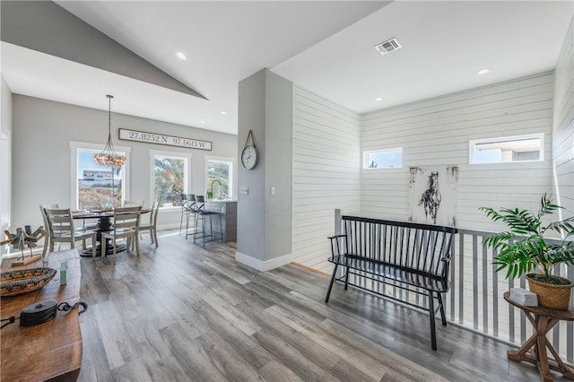 corridor featuring wood-type flooring, wood walls, a notable chandelier, and vaulted ceiling