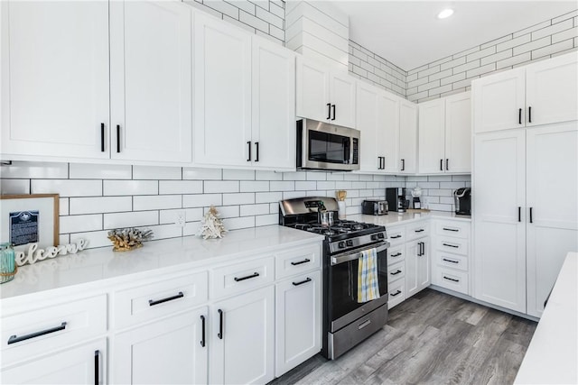 kitchen with decorative backsplash, white cabinets, wood-type flooring, and appliances with stainless steel finishes