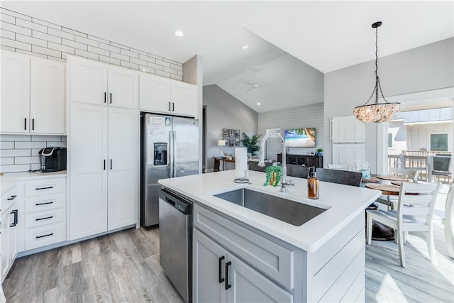 kitchen with white cabinets, appliances with stainless steel finishes, sink, hanging light fixtures, and a center island with sink