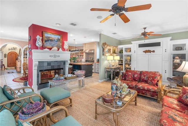 tiled living room with a tiled fireplace, ceiling fan, and ornamental molding