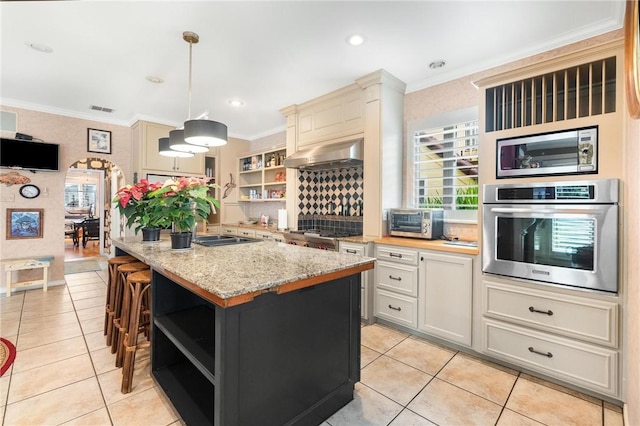 kitchen featuring stainless steel appliances, ventilation hood, decorative light fixtures, a kitchen island, and ornamental molding