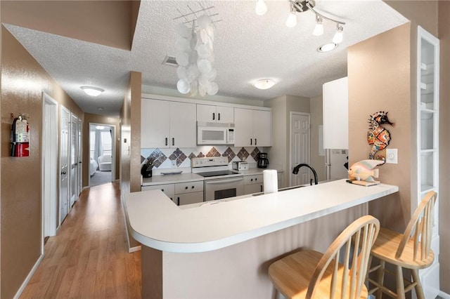 kitchen with white appliances, a breakfast bar, white cabinets, kitchen peninsula, and light wood-type flooring