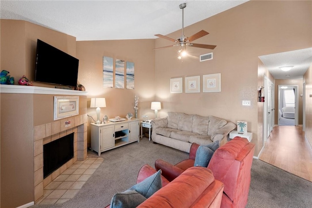 living room featuring ceiling fan, light colored carpet, high vaulted ceiling, and a tile fireplace