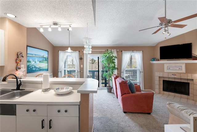 kitchen with sink, a tile fireplace, white cabinetry, light carpet, and vaulted ceiling