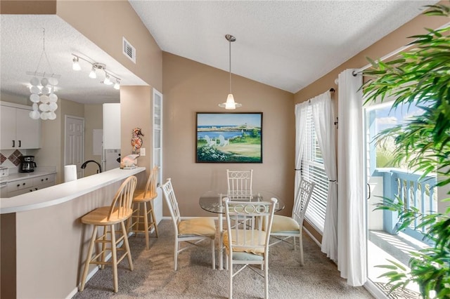 dining space featuring lofted ceiling, sink, light carpet, and a textured ceiling