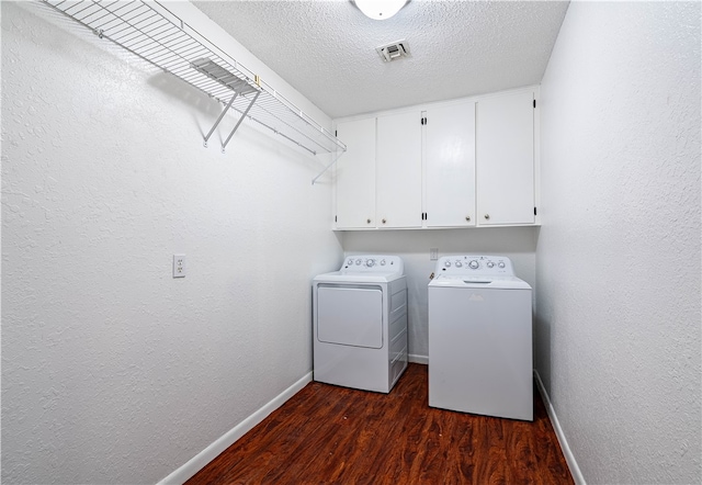 clothes washing area with cabinets, a textured ceiling, washing machine and dryer, and dark hardwood / wood-style floors