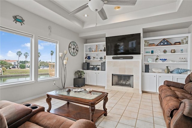 living area featuring a tiled fireplace, built in shelves, light tile patterned flooring, and a raised ceiling