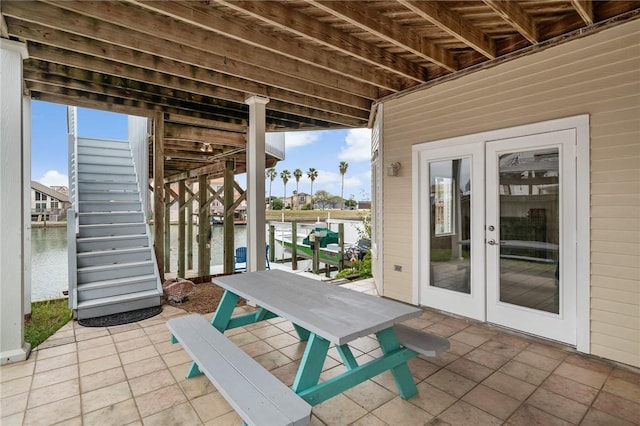 view of patio / terrace with french doors, a water view, a boat dock, and stairs