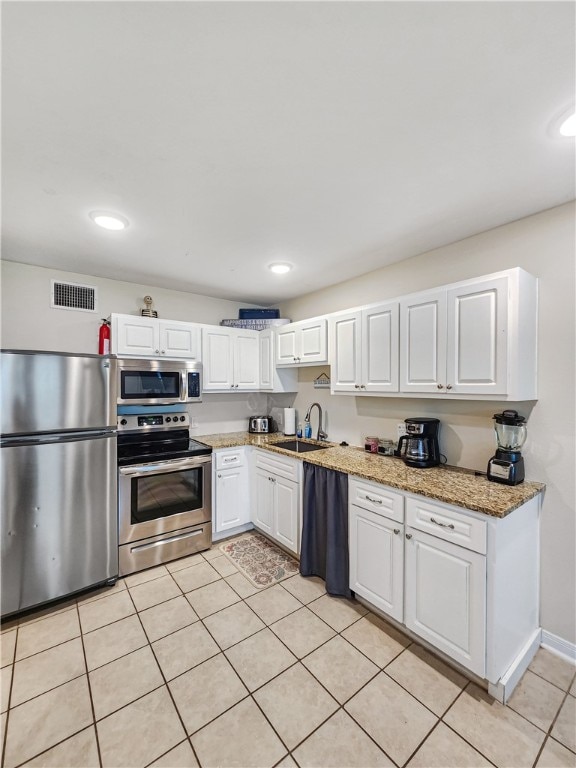 kitchen featuring stainless steel appliances, light tile patterned flooring, white cabinetry, and light stone countertops