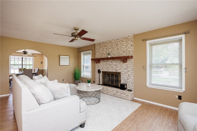 living room featuring a stone fireplace, light hardwood / wood-style flooring, and ceiling fan