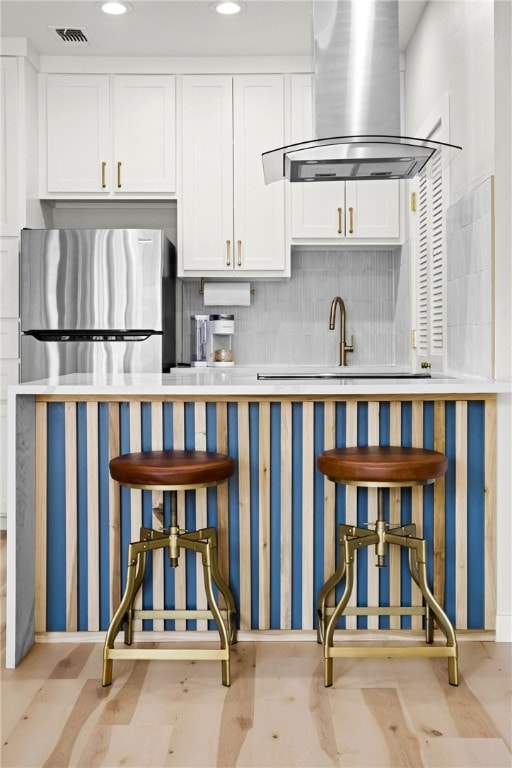 kitchen with exhaust hood, white cabinets, sink, decorative backsplash, and stainless steel fridge