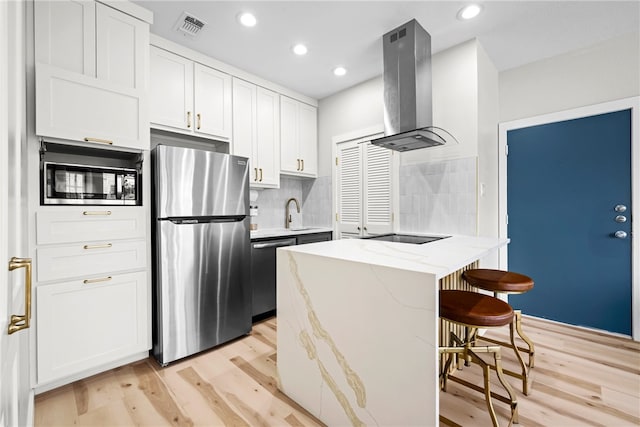 kitchen with white cabinets, decorative backsplash, light wood-type flooring, appliances with stainless steel finishes, and island range hood