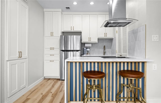 kitchen featuring a kitchen bar, stainless steel refrigerator, island range hood, and white cabinets