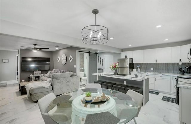 dining space with ceiling fan with notable chandelier and a barn door