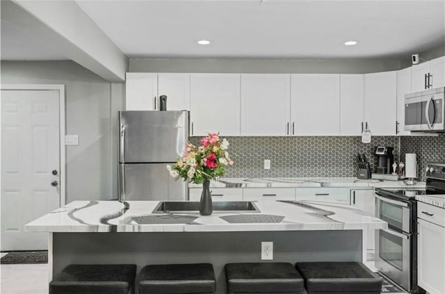 kitchen with appliances with stainless steel finishes, a kitchen island, white cabinetry, tasteful backsplash, and a breakfast bar area