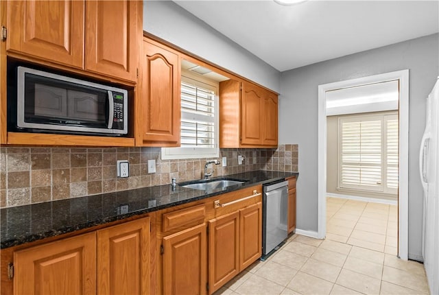 kitchen with stainless steel appliances, a sink, dark stone counters, and decorative backsplash