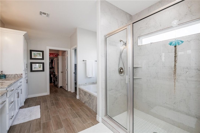 full bath featuring a walk in closet, visible vents, wood tiled floor, a shower stall, and vanity