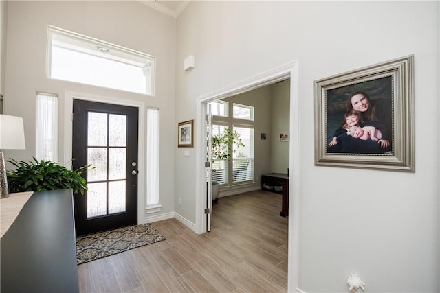 foyer entrance featuring light wood finished floors, a high ceiling, baseboards, and crown molding