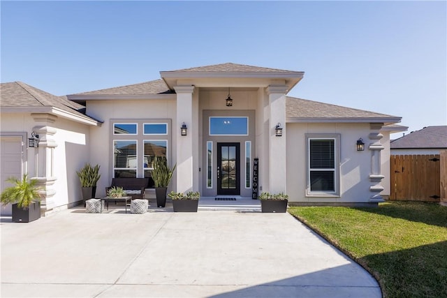 entrance to property featuring a yard, a shingled roof, fence, and stucco siding