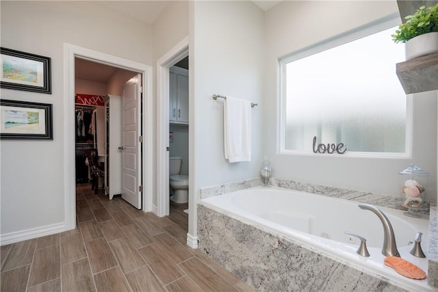 bathroom with toilet, wood finish floors, baseboards, a spacious closet, and a bath