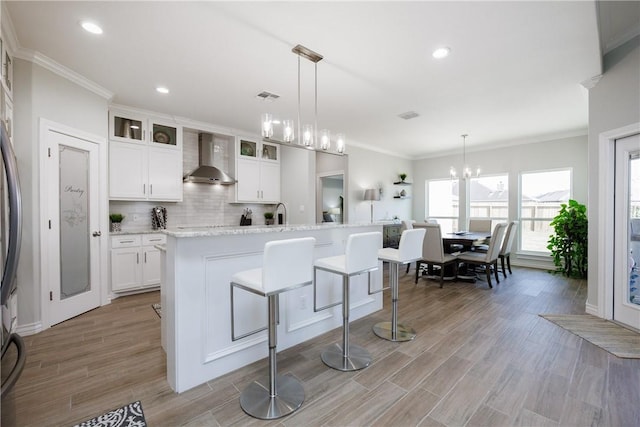 kitchen with tasteful backsplash, white cabinets, light wood-style floors, glass insert cabinets, and wall chimney range hood