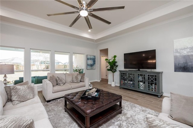 living room featuring ceiling fan, wood finished floors, baseboards, ornamental molding, and a raised ceiling