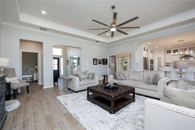 living area with a tray ceiling, wood finish floors, visible vents, and crown molding