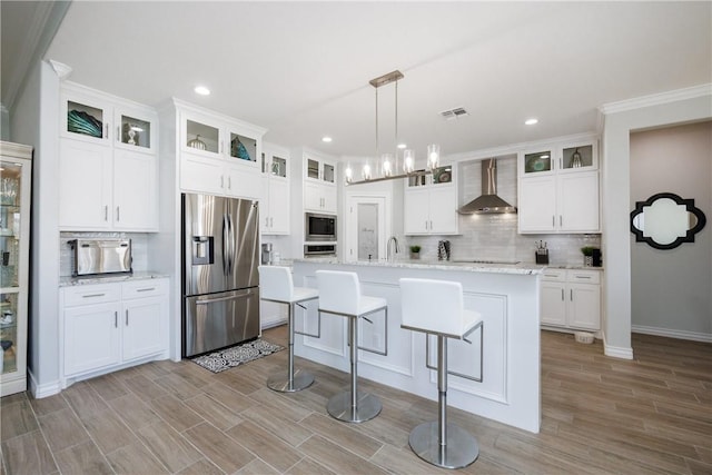 kitchen with wall chimney range hood, white cabinetry, stainless steel appliances, and decorative backsplash