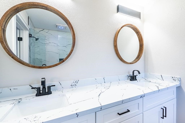 full bathroom with a sink, a marble finish shower, and double vanity