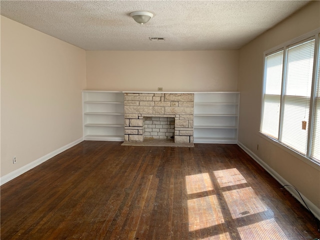 unfurnished living room featuring a textured ceiling, a fireplace, visible vents, baseboards, and dark wood-style floors