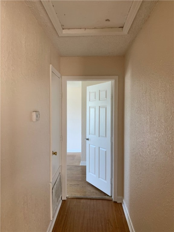 corridor with dark wood-style flooring, visible vents, a textured wall, and baseboards