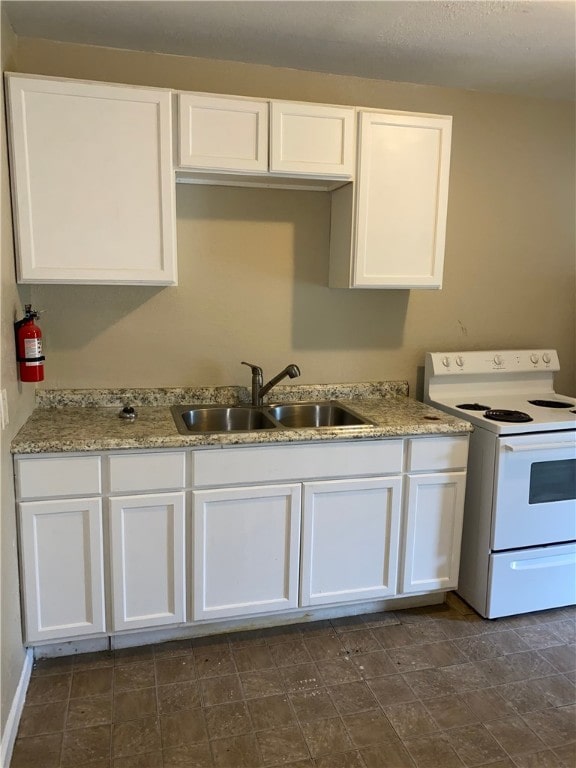 kitchen with light stone counters, white range with electric cooktop, a sink, and white cabinets