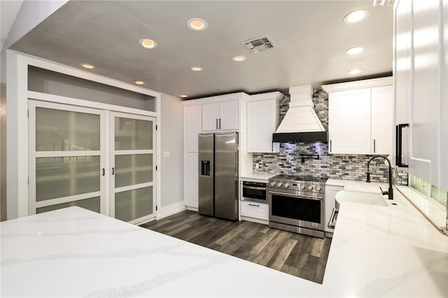 kitchen with light stone countertops, custom exhaust hood, white cabinets, appliances with stainless steel finishes, and sink