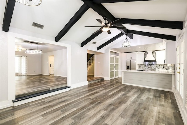 unfurnished living room featuring vaulted ceiling with beams, ceiling fan with notable chandelier, and hardwood / wood-style flooring