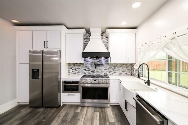 kitchen with appliances with stainless steel finishes, dark hardwood / wood-style flooring, white cabinets, and premium range hood