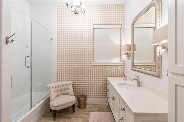 bathroom with enclosed tub / shower combo, wood finished floors, vanity, and wallpapered walls