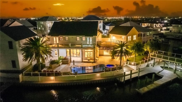 back of house at night featuring a balcony, a patio area, and an outdoor pool